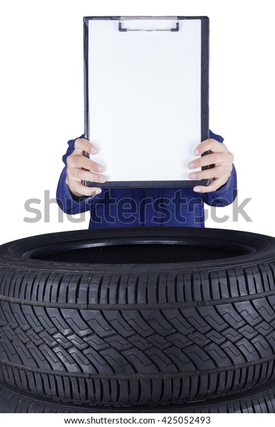 Image of a male mechanic showing empty\
clipboard above tires, isolated on white\
background