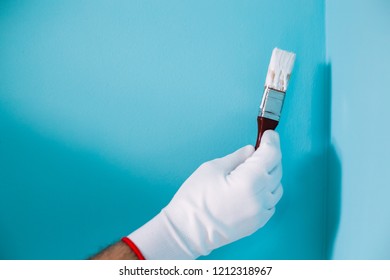 Image Of Man Holding Paintbrush In Front Of Blue Wall.