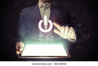 Image Of A Man With Tablet Pc In His Hands. Finger Touches The Power Button Icon. ON- OFF Concept Of Something.