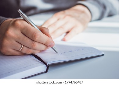 An image of a man's hand writing the phrase "I can do it!"in a Notepad with a ballpoint pen. The man is sitting at a white table and is dressed in a gray jacket - Shutterstock ID 1794765487
