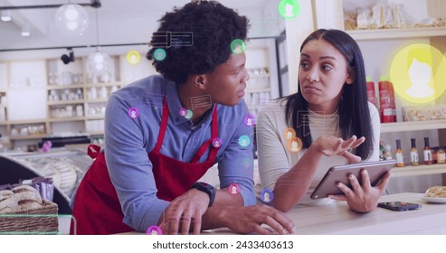 Image of media icons over diverse shop assistant and customer talking. Global business and digital interface concept digitally generated image. - Powered by Shutterstock