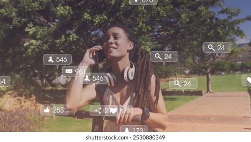 Image of media icons over smiling biracial woman with scooter talking on smartphone in park. health and fitness concept digitally generated image. - Powered by Shutterstock