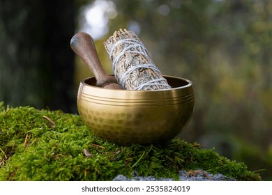 An image of a meditation singing bowl with white sage smudge stick resting on thick green moss in nature. - Powered by Shutterstock