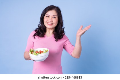 Image Of Middle Aged Asian Woman Eating Salad On Blue Background