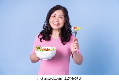 Image Of Middle Aged Asian Woman Eating Salad On Blue Background