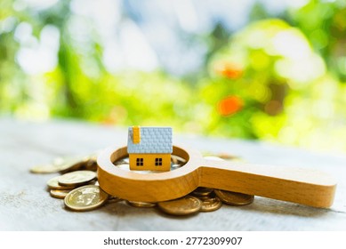 The image from the mirrorless camera show a magnifying glass with searching and home model put on the gold coin in the public park, Loan for real estate or saving money for buy a new house concept.