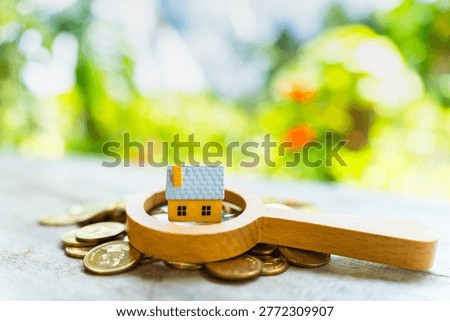 The image from the mirrorless camera show a magnifying glass with searching and home model put on the gold coin in the public park, Loan for real estate or saving money for buy a new house concept.