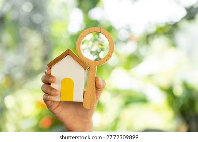 The image from the mirrorless camera show a Man hand hold the magnifying glass with searching and home model in the public park, Loan for real estate or saving money for buy a new house concept.