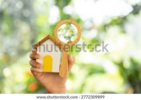 The image from the mirrorless camera show a Man hand hold the magnifying glass with searching and home model in the public park, Loan for real estate or saving money for buy a new house concept.