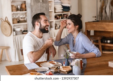 Image Of Modern Brunette Couple Man And Woman 20s Eating Breakfast Together While Sitting At Table At Home