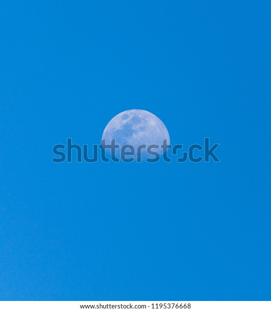 image of moon during daytime with bright blue\
sky in background
