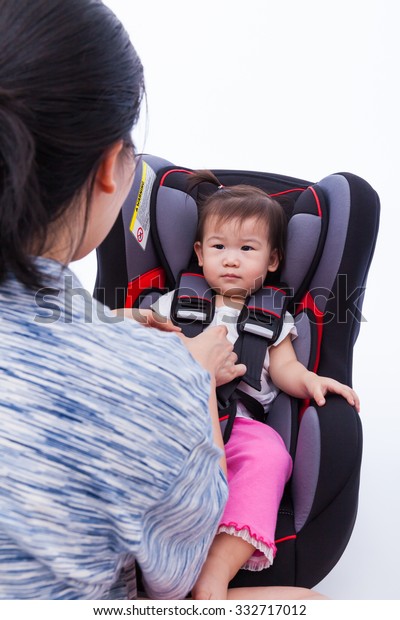 Image of Mother fasten\
with security belt to her little asian (thai) girl in safety\
car-seat, on white background. Concept about vehicle safety, symbol\
of protection, care