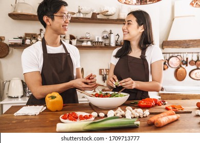 Image of multicultural couple smiling and looking on you while cooking dinner in cozy kitchen - Powered by Shutterstock