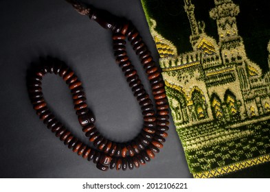 An image of Muslim Tasbih Prayer Beads Palm Seeds Islamic Prayer Zikr Misbaha and prayer mat isolated with black background.