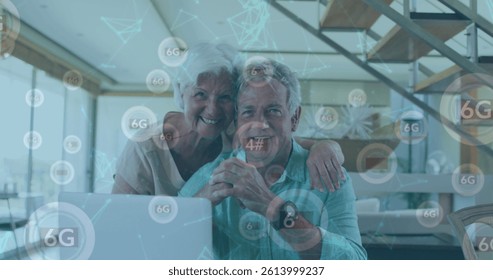 Image of network of connections with icons over senior caucasian couple using laptop. global connections, digital interface and technology concept digitally generated image.