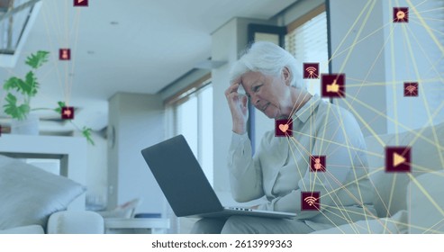 Image of network of connections with icons over worried senior caucasian woman using laptop. global connections, digital interface and technology concept digitally generated image.