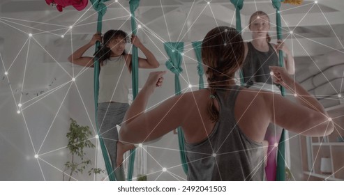 Image of network over diverse female instructor and teenager girls practicing aerial yoga. Wellbeing, energy, healthy lifestyle, connection and communication, digitally generated image. - Powered by Shutterstock