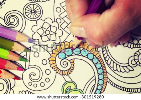 An image of a new trendy thing called adults coloring book with a vintage twist. In this image a person is coloring an illustrative and detailed pattern for stress relieve for adults.