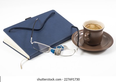Image of notebook coffee cup closed pen and glasses.