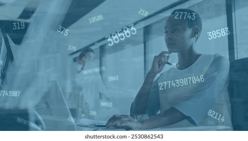 Image of numbers changing over afrcan american woman with computer in office. Business, finance, economy, data processing and technology concept digitally generated image.
