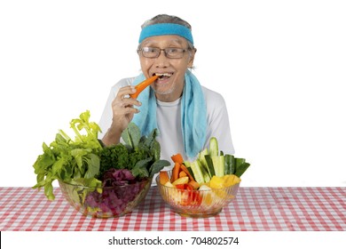 Image Of An Old Man Wearing Sportswear While Eating Organic Vegetables, Isolated On White Background