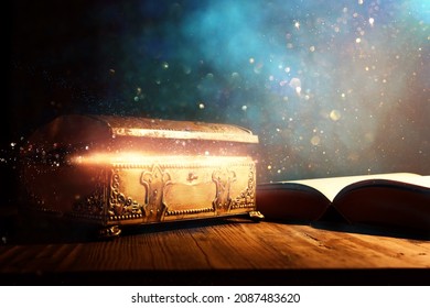 image of open antique book and gold treasure chest on wooden table with glitter overlay