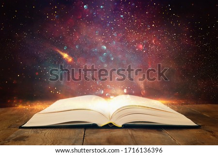 image of open antique book on wooden table with glitter overlay