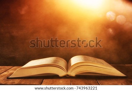 image of open antique book on wooden table with glitter background