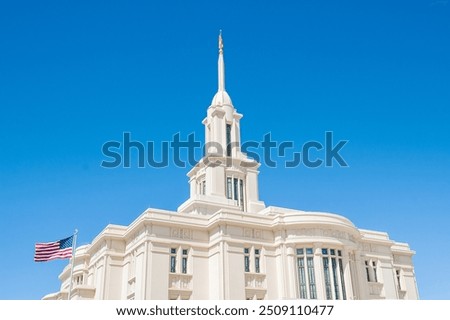 Image of the Payson, UT LDS temple with the American flag flying in front of it and the bright, blue sky behind it. White Mormon temple in Payson. 