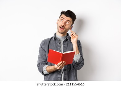 Image Of Pensive Young Man Writing Down Ideas In Planner, Looking Thoughtful At Logo And Scratching Ear With Pen, Holding Journal In Hands, White Background