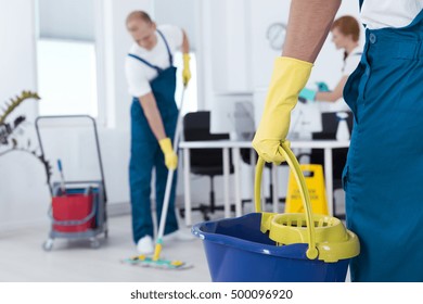 Image of person holding mop pail and man cleaning floor