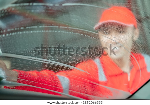 image photo from\
inside a car cleaning car Asian man wearing a uniform cleaning the\
side glass in a car salon