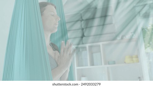 Image of plant leaves over happy caucasian woman meditating at aerial yoga class. Yoga, wellbeing, meditation, meditation and tranquility, digitally generated image. - Powered by Shutterstock