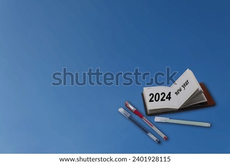 An image of a pocketbook with open pages for the New Year with a pen on the side on a blue background.
