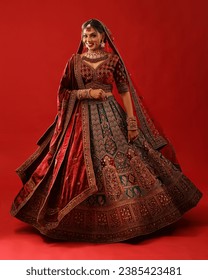 The image portrays a beautiful Indian woman dressed in a traditional red and green lehenga.
					The woman is posing with a bright smile on her face.he background of the picture is a deep red color.