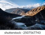 The image portrays a dramatic landscape where a river winds its way through a steep, rugged valley. The river appears to split and rejoin, creating a dynamic flow pattern amidst the rocky terrain. 