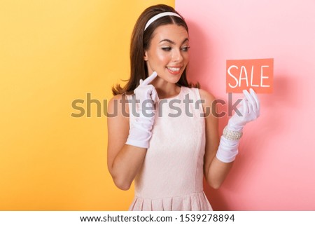 Image of a positive optimistic happy pin-up woman in dress isolated over double-colored yellow pink background holding sale blank.