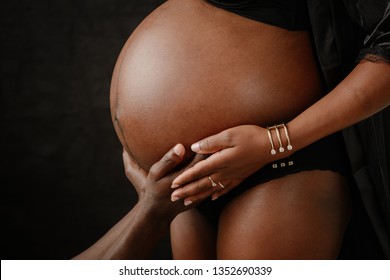 Image of pregnant  Afro American couple. Husband touching his wife belly with hands. black background