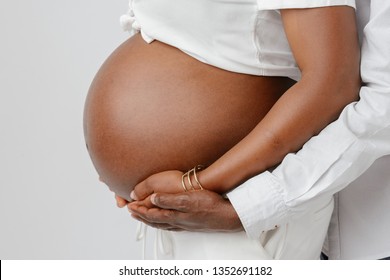 Image of pregnant  Afro American couple. Husband touching his wife belly with hands. 