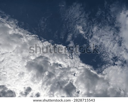 The image presents a dramatic, close-up skyward shot showing a distinct dividing line between two different cloud formations and sky conditions.

Foreground and Lower Half: Dense, thick, and billowy white-and-gray cumulus clouds occupy the lower section of the frame, showing heavy texture, depth, and shadowy highlights.

​Background and Upper Half: 
A deep navy-blue sky stretches across the top portion, covered with thin, wispy, feathered altocumulus clouds that create a sheer, textured veil over the dark backdrop.