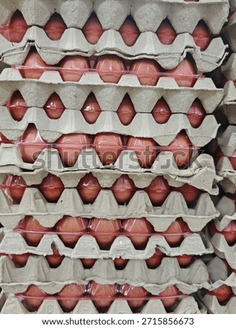 The image presents a front-facing, full-frame view of brown chicken eggs stored in stacked, recycled paper pulp trays. Each row of eggs is partially covered by a thin, red-tinted plastic wrap, creating a rhythmic pattern of pointed oval shapes. The contrast between the rough, grey texture of the eco-friendly cardboard trays and the smooth, glossy surface of the eggs highlights a systematic approach to retail storage and mass distribution in a supermarket environment.