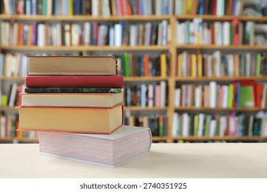 The image presents a warm, softly lit scene centered on a small stack of books with a handful of colored pencils resting on top. The composition uses a shallow depth of field, creating a pleasing blur in the background that suggests tall bookshelves filled with more books. The overall atmosphere feels calm, studious, and inviting—like a quiet corner of a library or a cozy study room. In the foreground, three thick hardcover books are stacked horizontally. Their covers appear in muted tones—beige, tan, and possibly a soft red or rust color along the edges. The pages are slightly textured, visible along the sides of the stack, giving a sense of weight and substance. 
Resting diagonally across the top book is a small cluster of sharpened colored pencils. The pencil tips point toward the viewer, making them the sharpest and most detailed element in the image. Their wooden casings are natural light brown, while the cores display various colors: yellow, orange, red, purple, green, blue, and white. 
