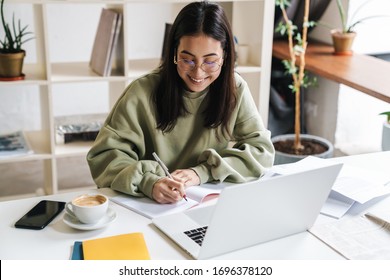 Image of a pretty positive optimistic young girl student using laptop computer indoors studying.