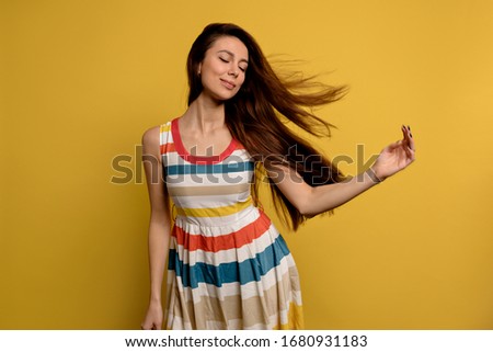 Image of a pretty smiling young woman in bright summer dress isolated over yellow wall background. Fashion portrait of pretty girl posing having fun over colorful wall