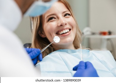 Image of pretty young woman sitting in dental chair at medical center while professional doctor fixing her teeth - Shutterstock ID 1389890039