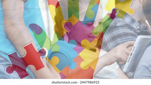 Image of puzzle pieces and hand over diverse schoolchildren using tablet. autism awareness month and celebration concept digitally generated image. - Powered by Shutterstock