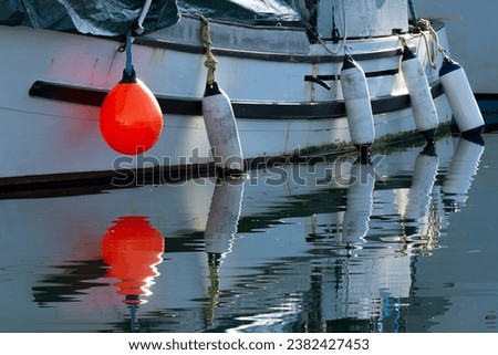 An image of a red buoy and fishing boat reflecting in clear ocean waters. 