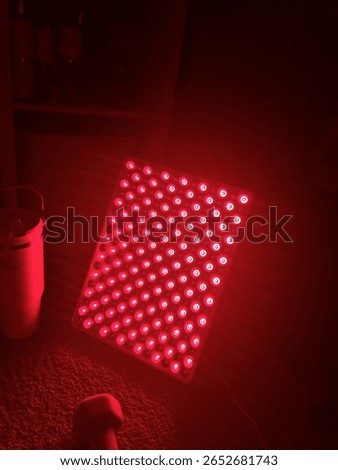 Image of a red light therapy lamp glowing onto a stanley cup and a handheld weight