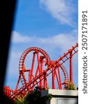 An image of a red rollercoaster track and the blue sky in the background in the amusement park.