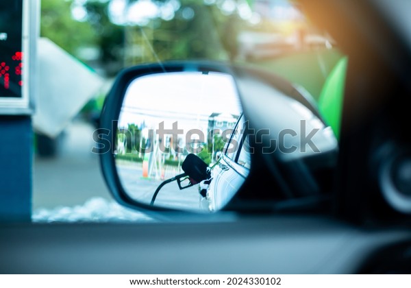 ฺBlurry image of\
refueling in side mirror of car. Side view mirror with  the fuel\
refueling service for the\
car.